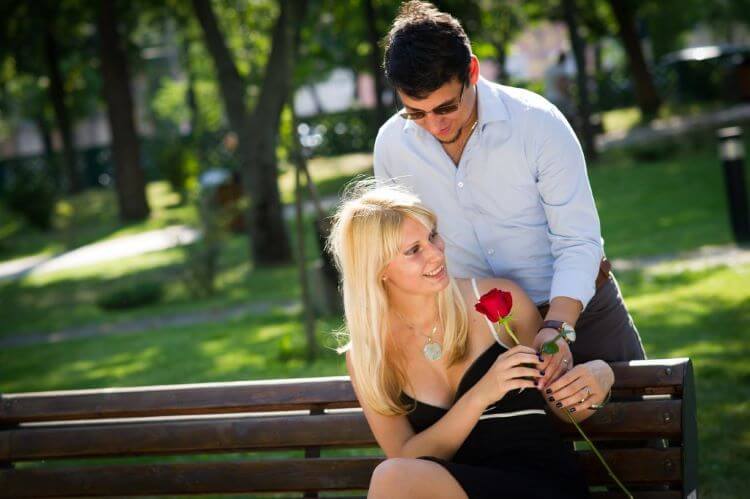ベンチに座っている女性に薔薇を渡す男性