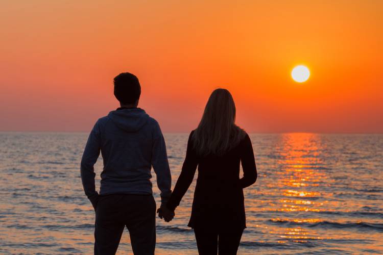 夕暮れ時に海辺で手をつなぐカップル